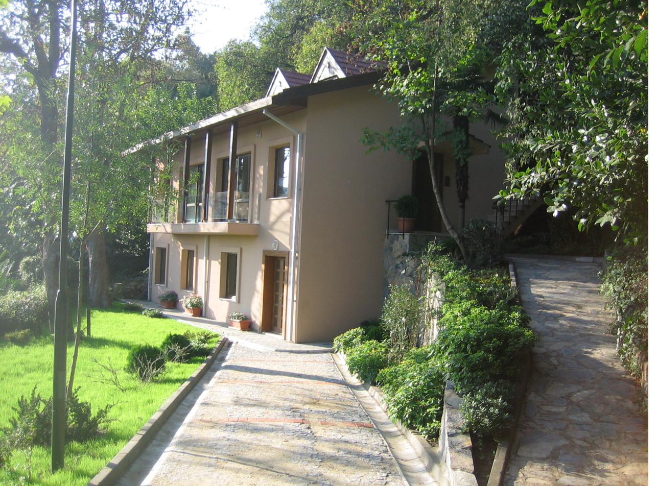 A two-storey house among trees on a wooded hillside, with a stone path leading to it.
